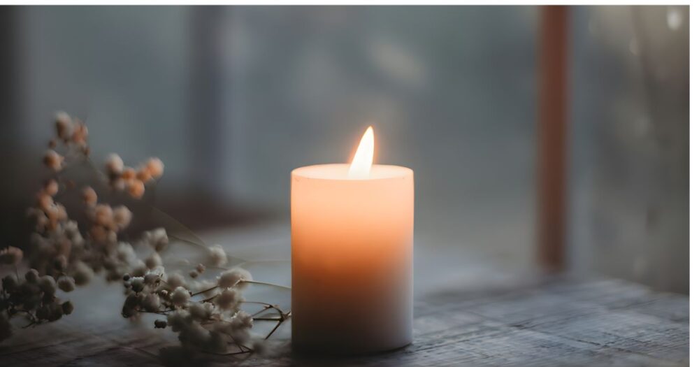 木のテーブルの上で静かに揺れるキャンドルの灯りと、そばに置かれた白い小花。