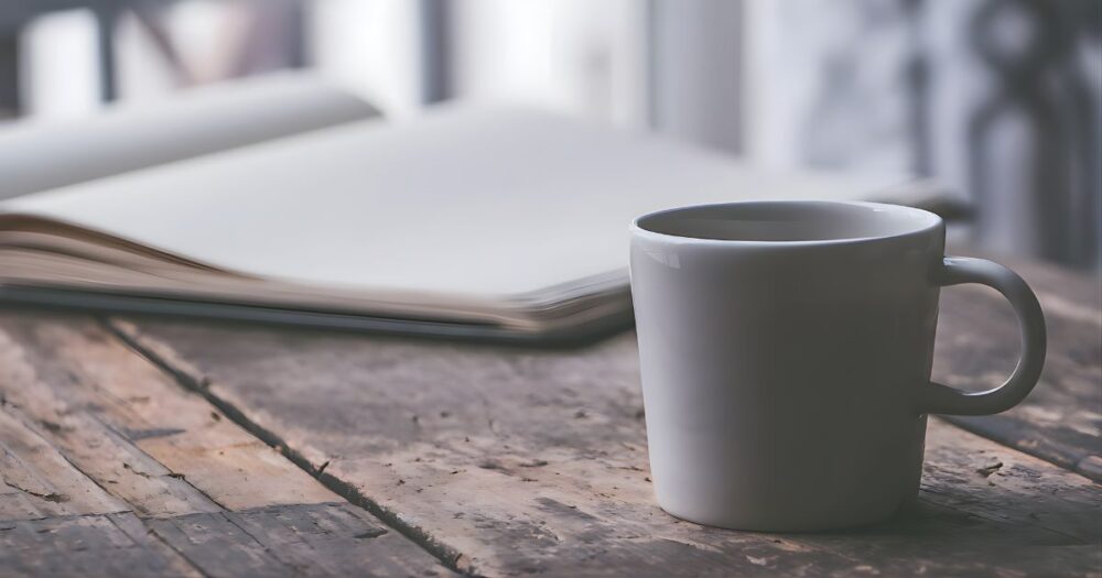 使い込まれた木のテーブルに置かれた、一客のマグカップと開かれたノート。一人の時間を心地よく過ごし、自分と向き合う自立したひとときを象徴するイメージ