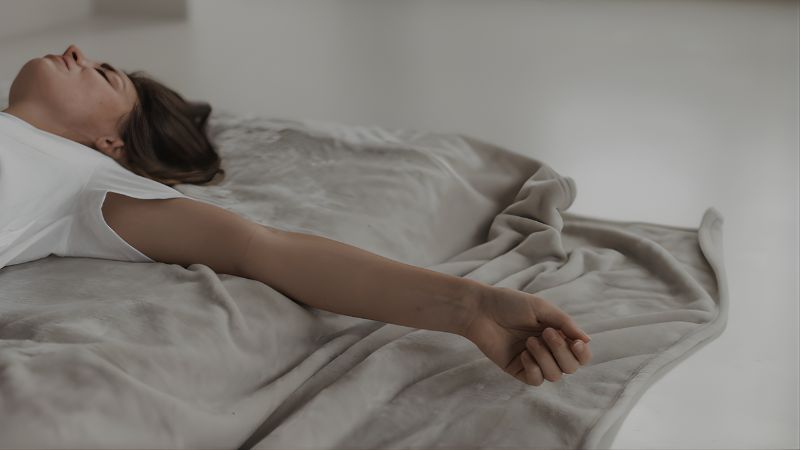 ベッドに横たわり、手の力が抜けた脱力した体のイメージ