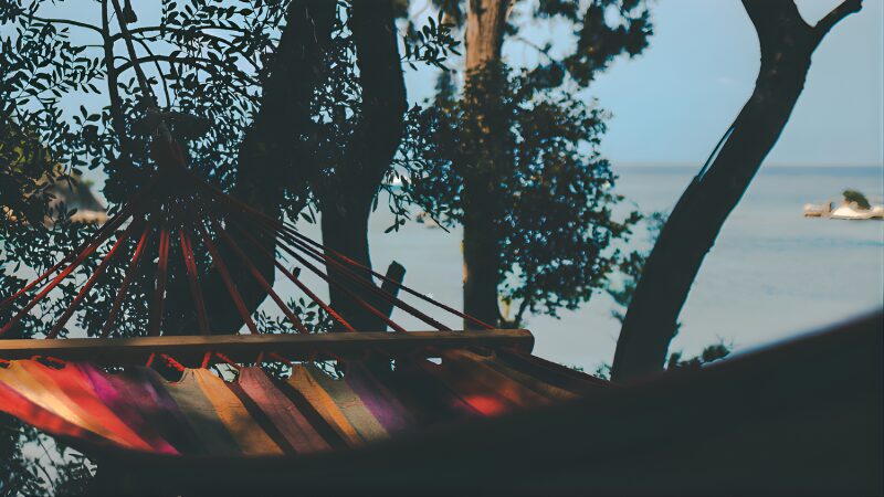 木陰に設置されたカラフルなハンモック越しに、穏やかな海が広がる風景
